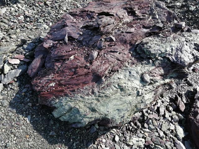 Gesteinsblock aus der Nähe: grüngrauer Grünstein, darüber eine rotviolette, blättrig zerfallende Aschenschicht